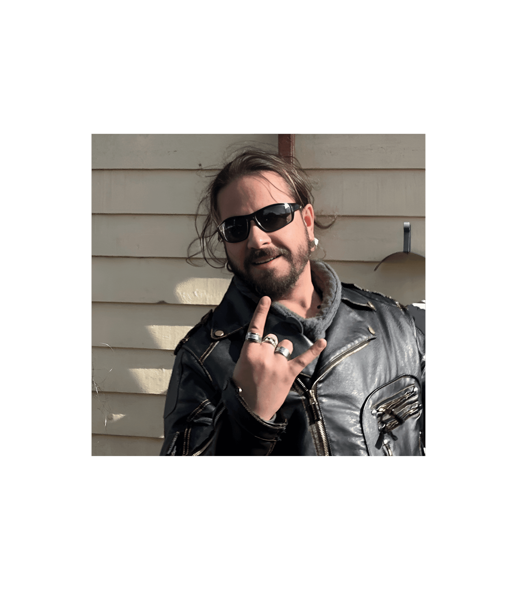 Person in a leather jacket and sunglasses making a rock hand gesture.